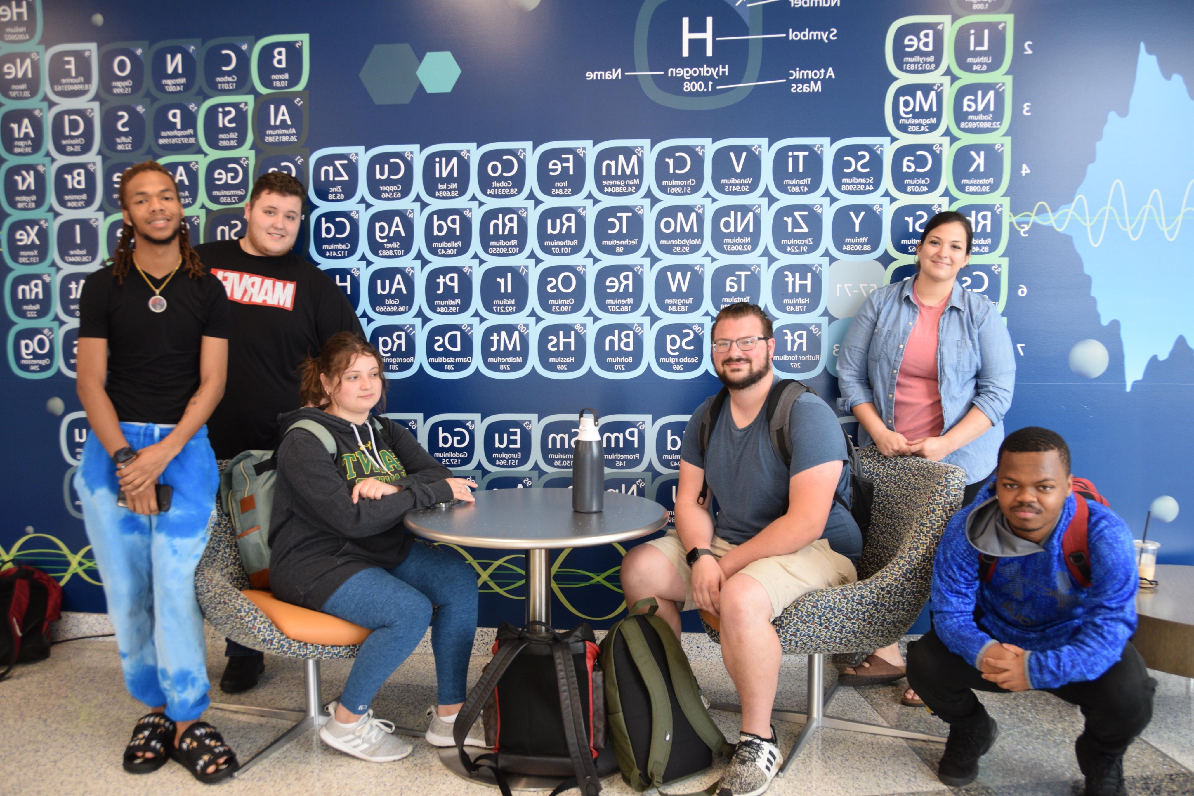 A group of students posing in front of the periodic table in Updike Hall