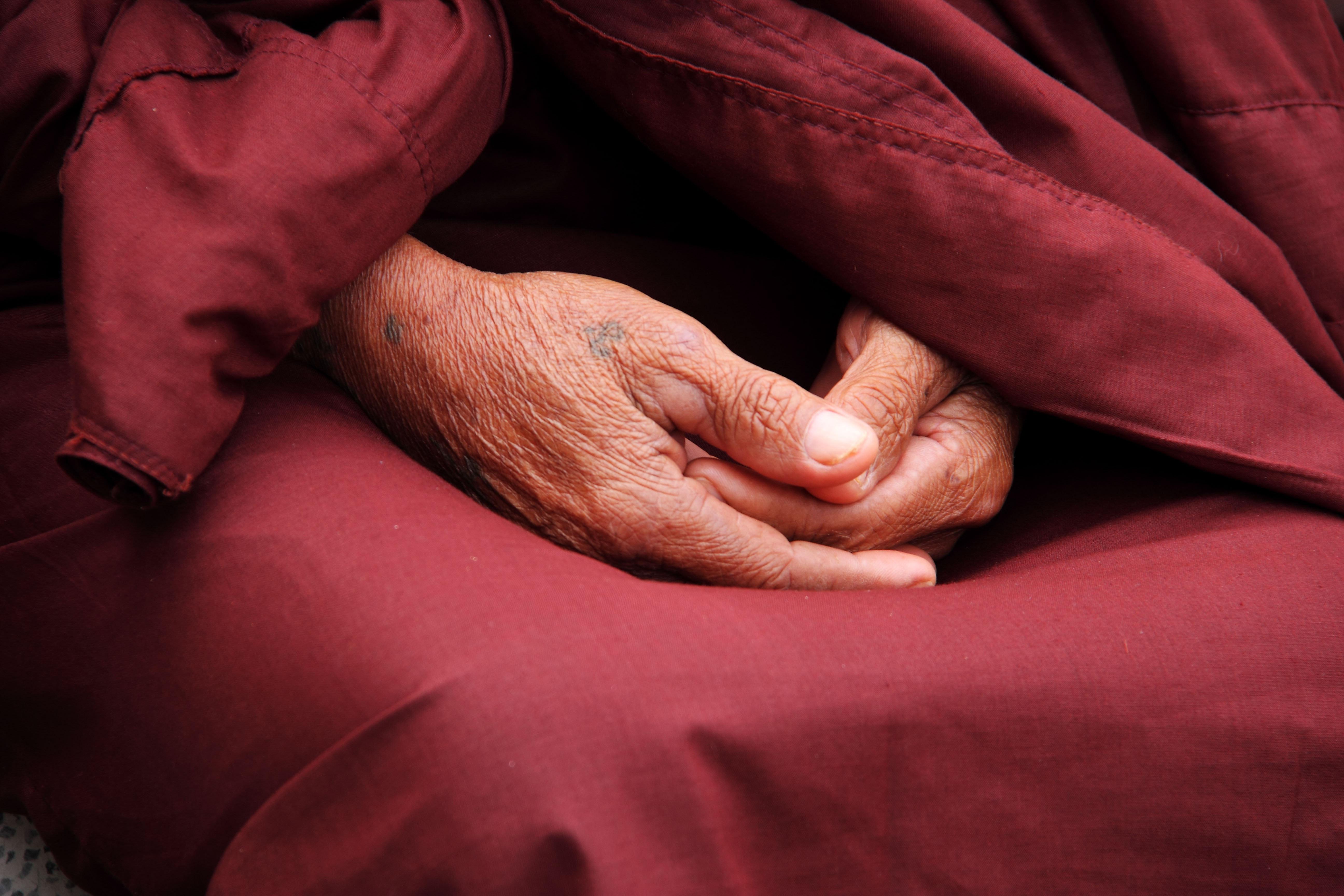 Monks hands in their lap with a marron robe